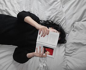 Frau liegt auf dem Bett und liest ein Buch